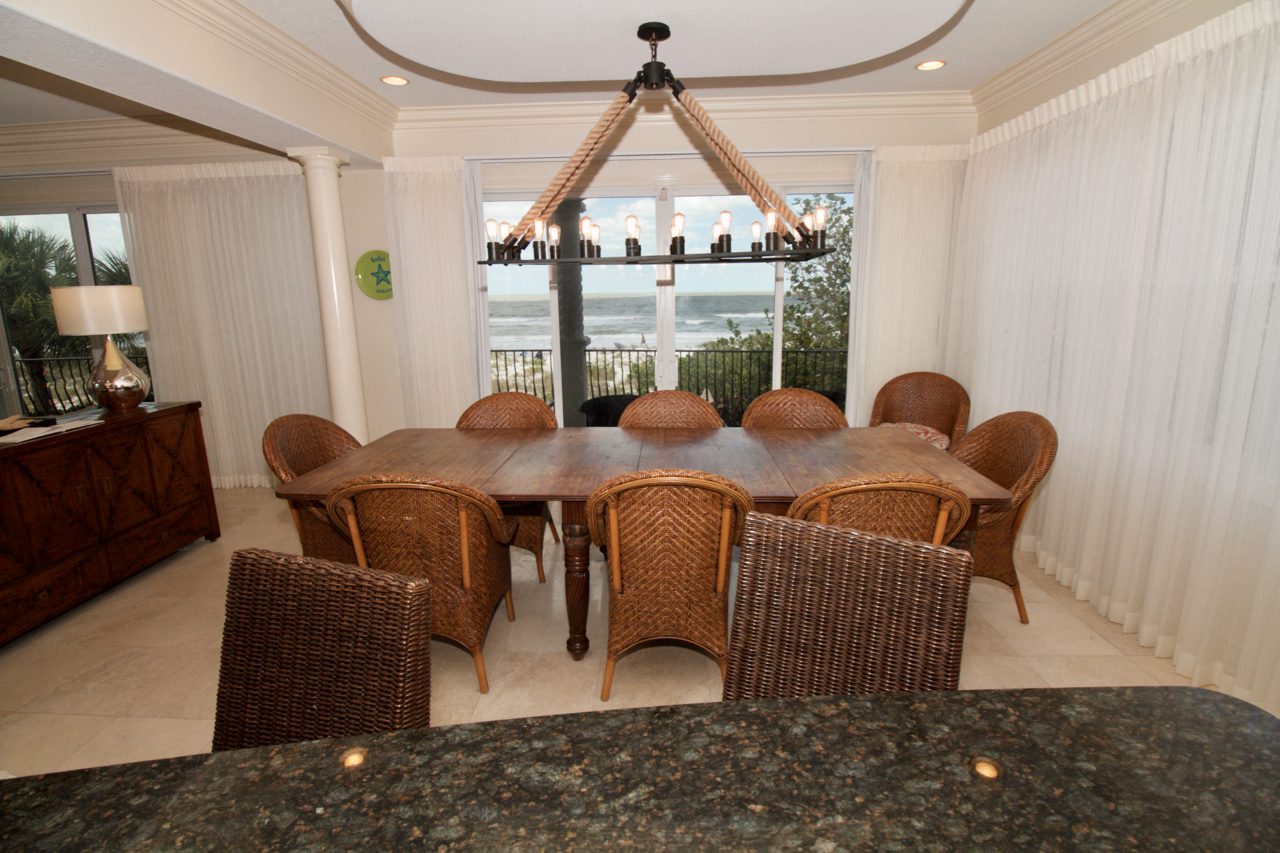 A large dining room table with chairs and a view of the ocean.