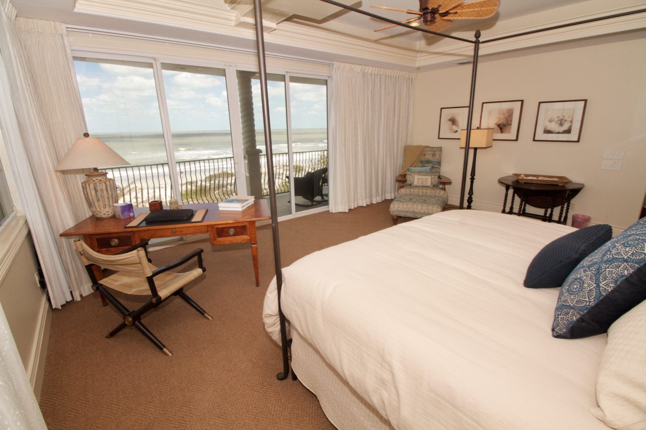 A bedroom with two beds and a balcony overlooking the ocean.